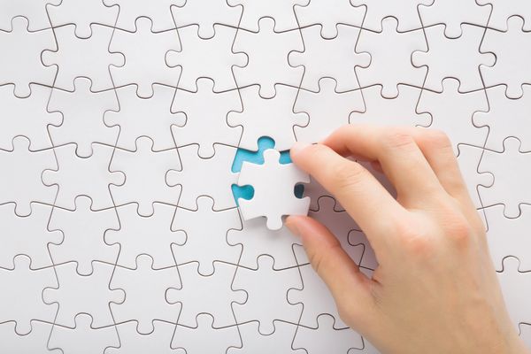 Hand placing the final white puzzle piece into a nearly completed puzzle.