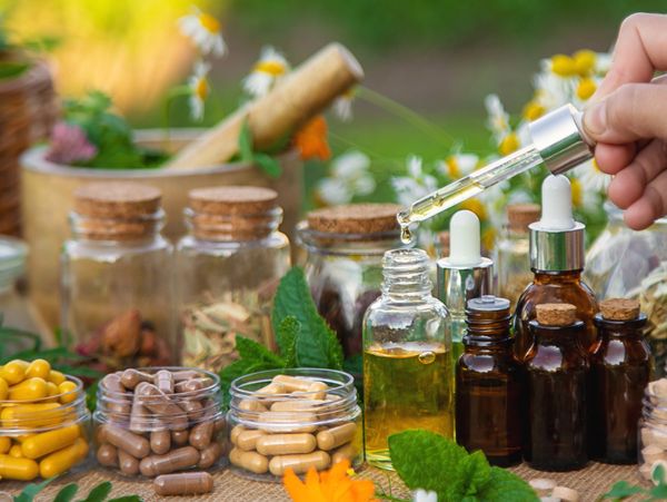 Various herbal supplements, capsules, and essential oils with a hand using a dropper.