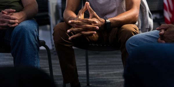 People sitting in a circle, hands clasped, suggesting a group meeting or discussion.
