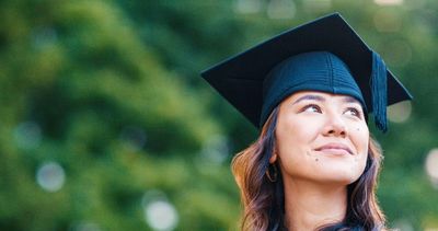 A woman in a graduation cap looking up happily.