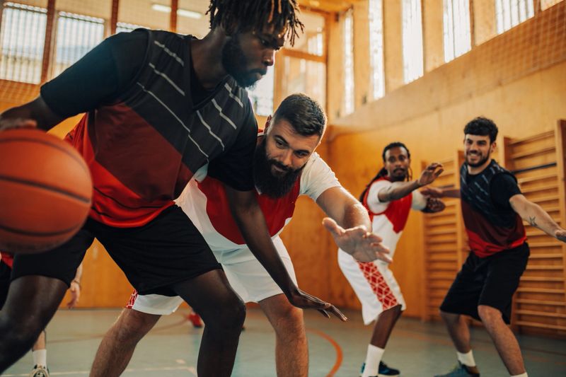 Multicultural team of professional sportsmen having basketball training on court indoors. An african american player is dribbling a ball. A professional basketball team in action on court has training