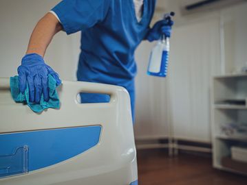 Healthcare worker disinfecting a hospital bed with gloves and spray.