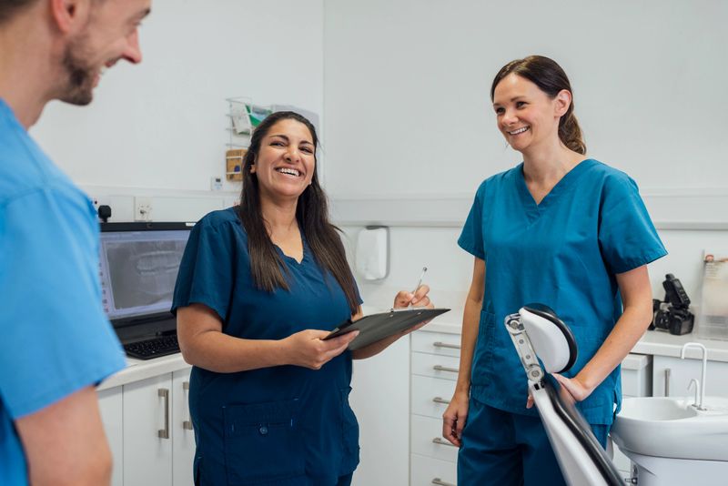 Dentists standing talking to one another while at a dentist practise in Newcastle Upon Tyne, North East England. They are wearing scrub uniforms.