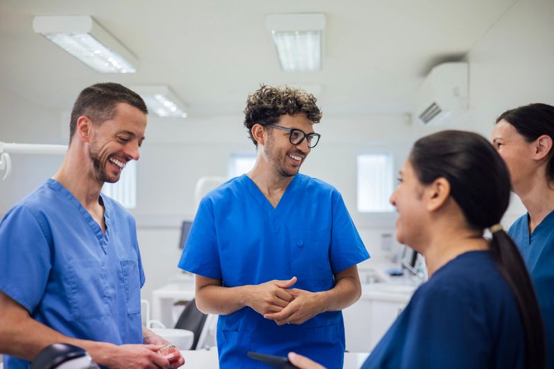 Dentists standing talking to one another while at a dentist practise in Newcastle Upon Tyne, North East England. They are wearing scrub uniforms.