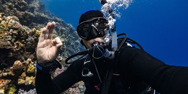 Scuba diver underwater near a coral reef giving an OK hand signal.