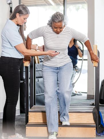 Physical therapist assists woman with step exercise in rehabilitation center.