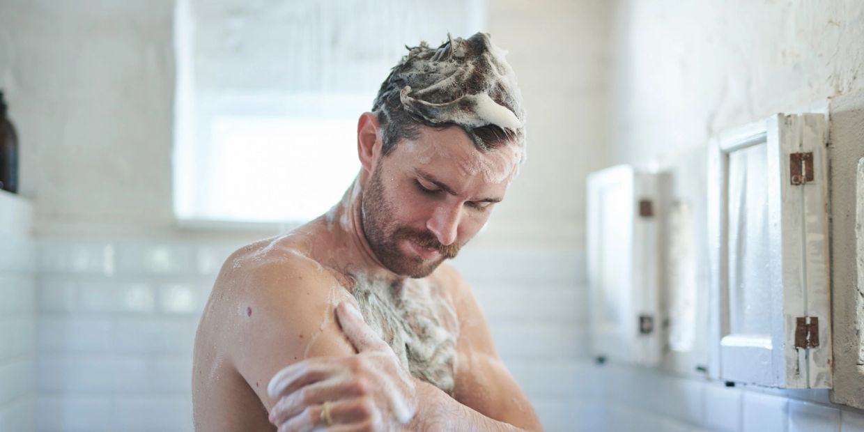 Man washing his body and hair with soap in a bathroom.