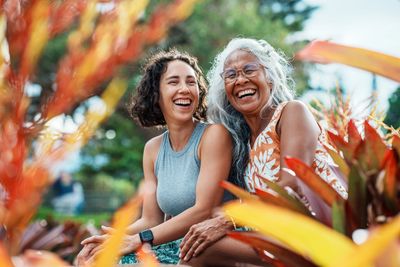 Two women joyfully laughing together outdoors among colorful foliage.