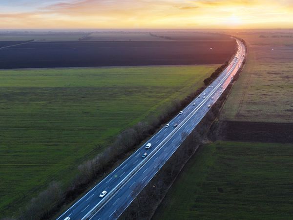 Highway cutting through farmland at sunset with light traffic.