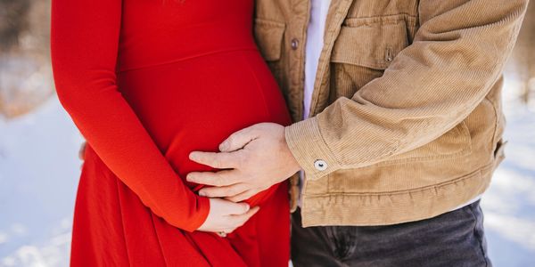 Couple lovingly holding pregnant belly outdoors.