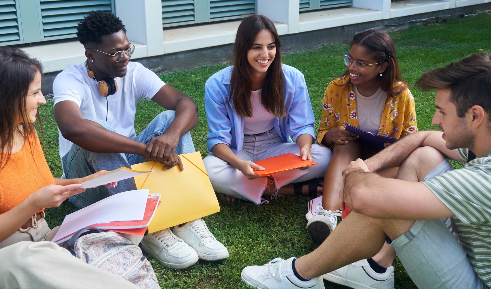 A diverse group of young people studying together outdoors on grass.