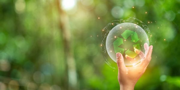 Hand holding a glowing sphere with a green recycling symbol against a blurred nature background.