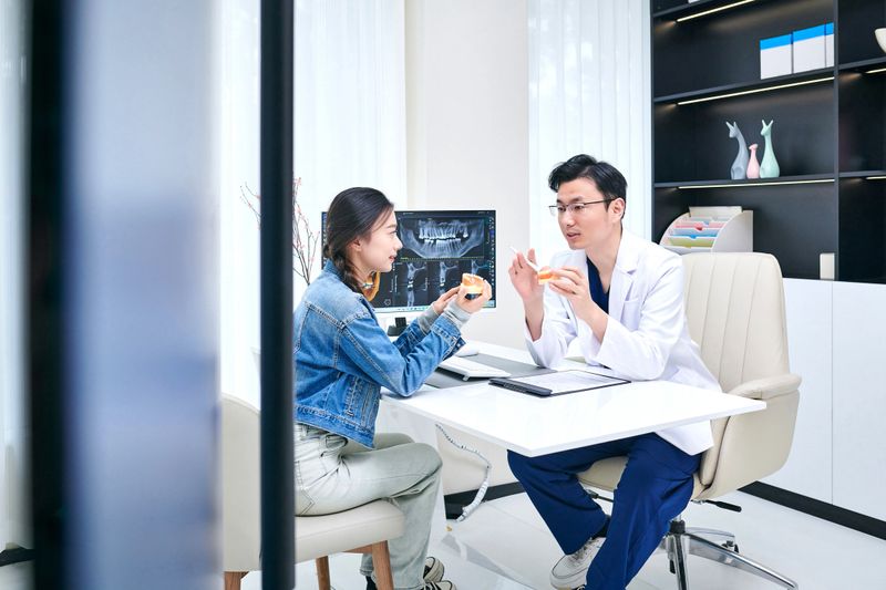 Asian dentist and female patient discussing dental x-ray image in dental office.
