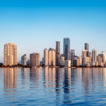 City skyline reflecting on calm water under a clear blue sky.