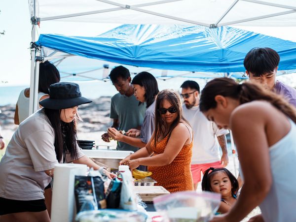 People preparing food under a blue canopy at an outdoor gathering.