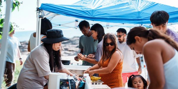 People gathered under a blue canopy preparing and serving food outdoors.