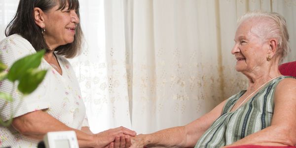 A caregiver holding hands with an elderly woman, sharing a warm moment.