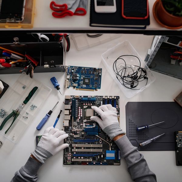 Hands with gloves assembling or repairing a computer motherboard on a desk.