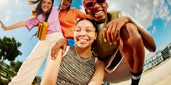 Four friends smiling and posing outdoors under a bright sky.