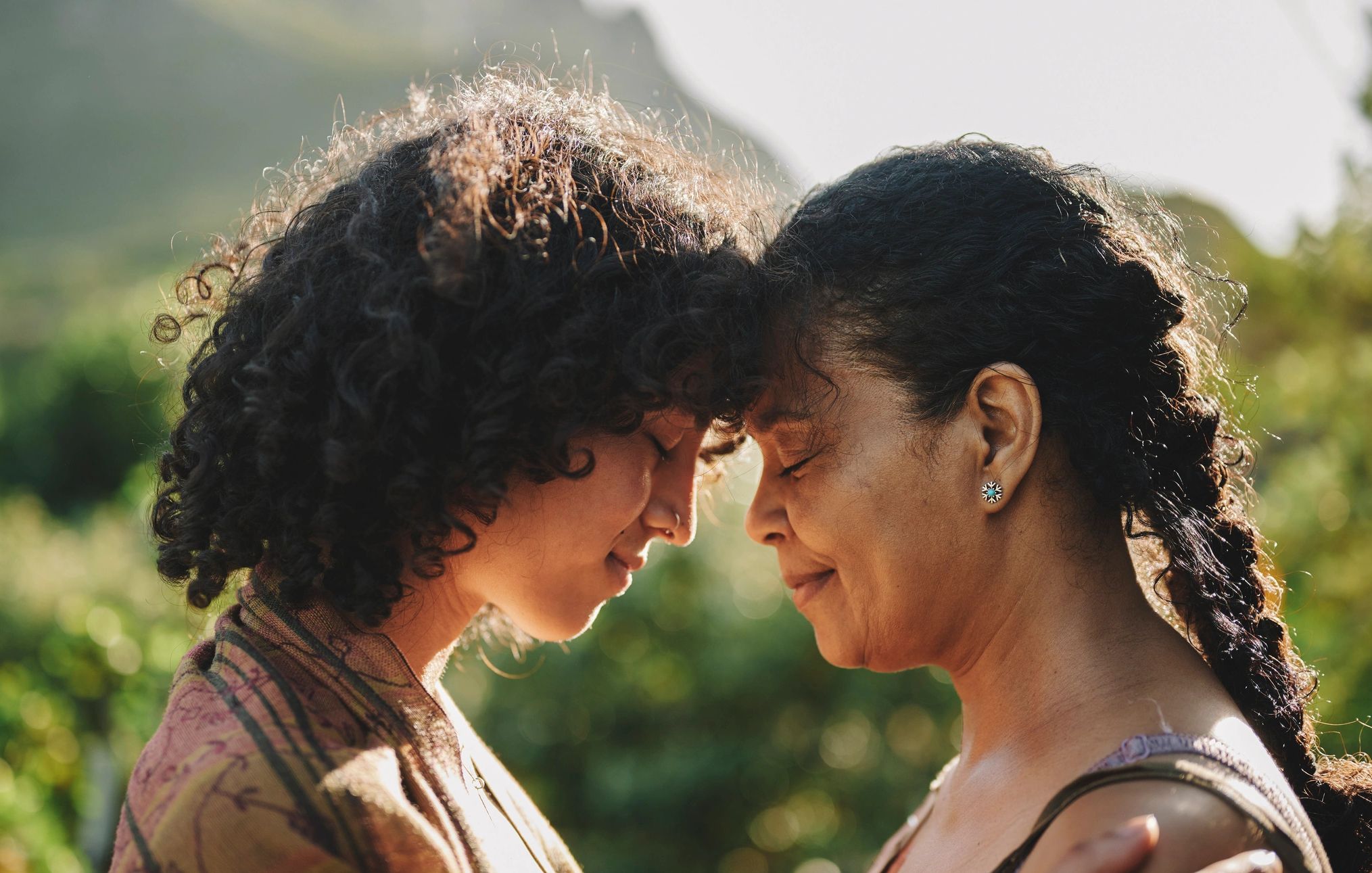 Two women touching foreheads outdoors, sharing a tender moment.