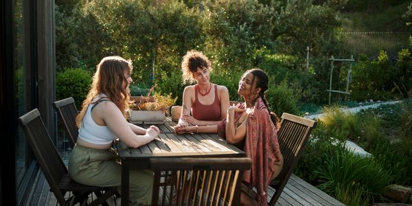 Three women enjoying a relaxed conversation outdoors on a wooden deck.