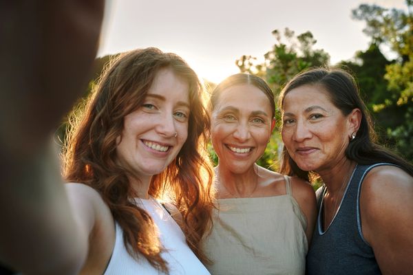 Three women smiling together outdoors at sunset.