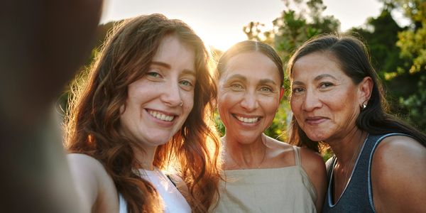 Three women smiling together outdoors at sunset.