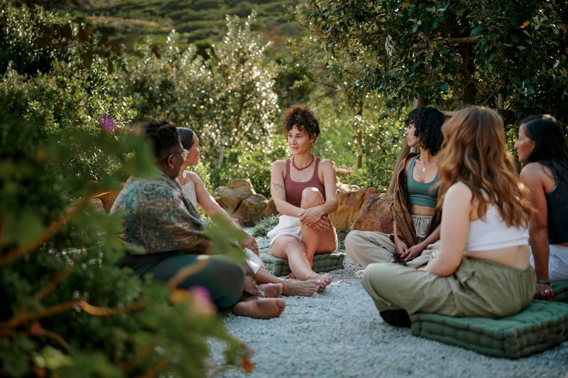 Diverse group of women talking while sitting together around a meeting area set outside in a scenic wellness retreat
