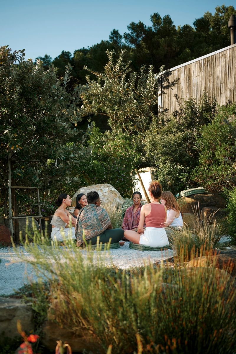 Smiling group of diverse women sitting outdoors in a circle and talking together in a meeting area set in a scenic wellness retreat