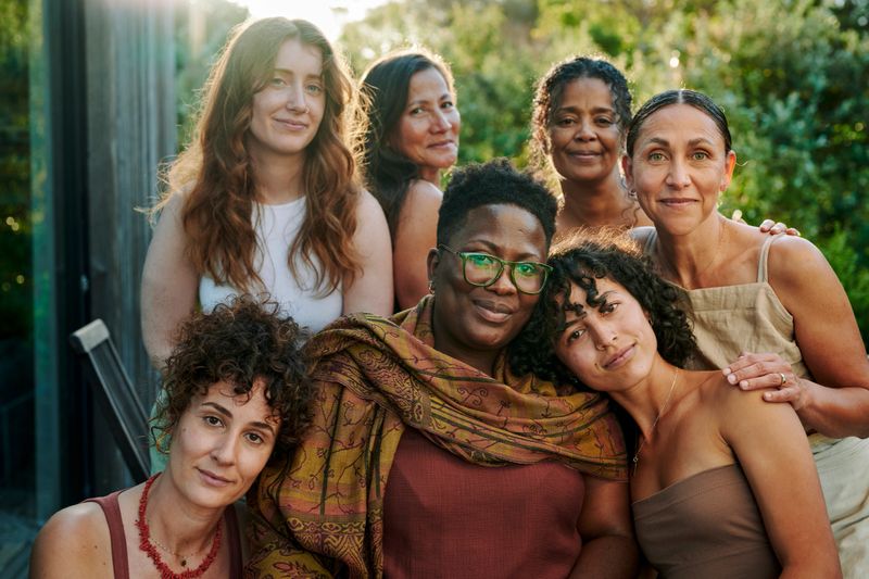 Portrait of a diverse group of supportive women smiling while sitting together outdoors on patio during a summer wellness retreat