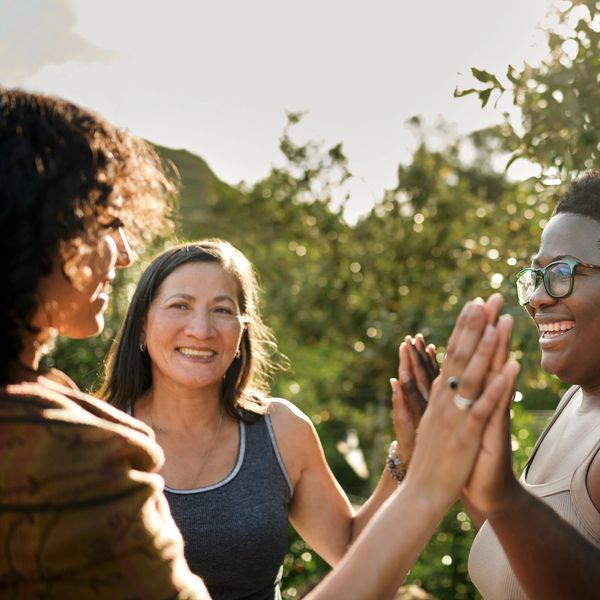 Three women smiling and high-fiving outdoors.