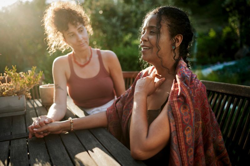 Diverse women supporting each other while talking around a table outside on a patio during a summer wellness retreat