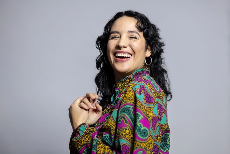 Portrait of attractive Latin woman with short hair. Female wearing colourful shirt laughing on grey background.