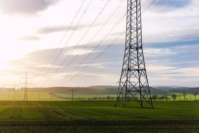 Electric transmission towers standing tall over green fields at sunset.