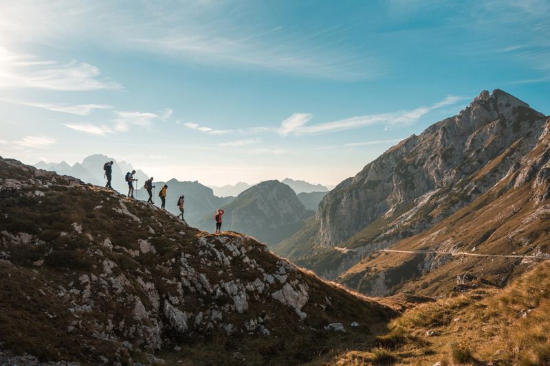 With backpacks and hiking poles, diverse friends trek together on a sunny day, embracing the joy of hiking in the mountains.