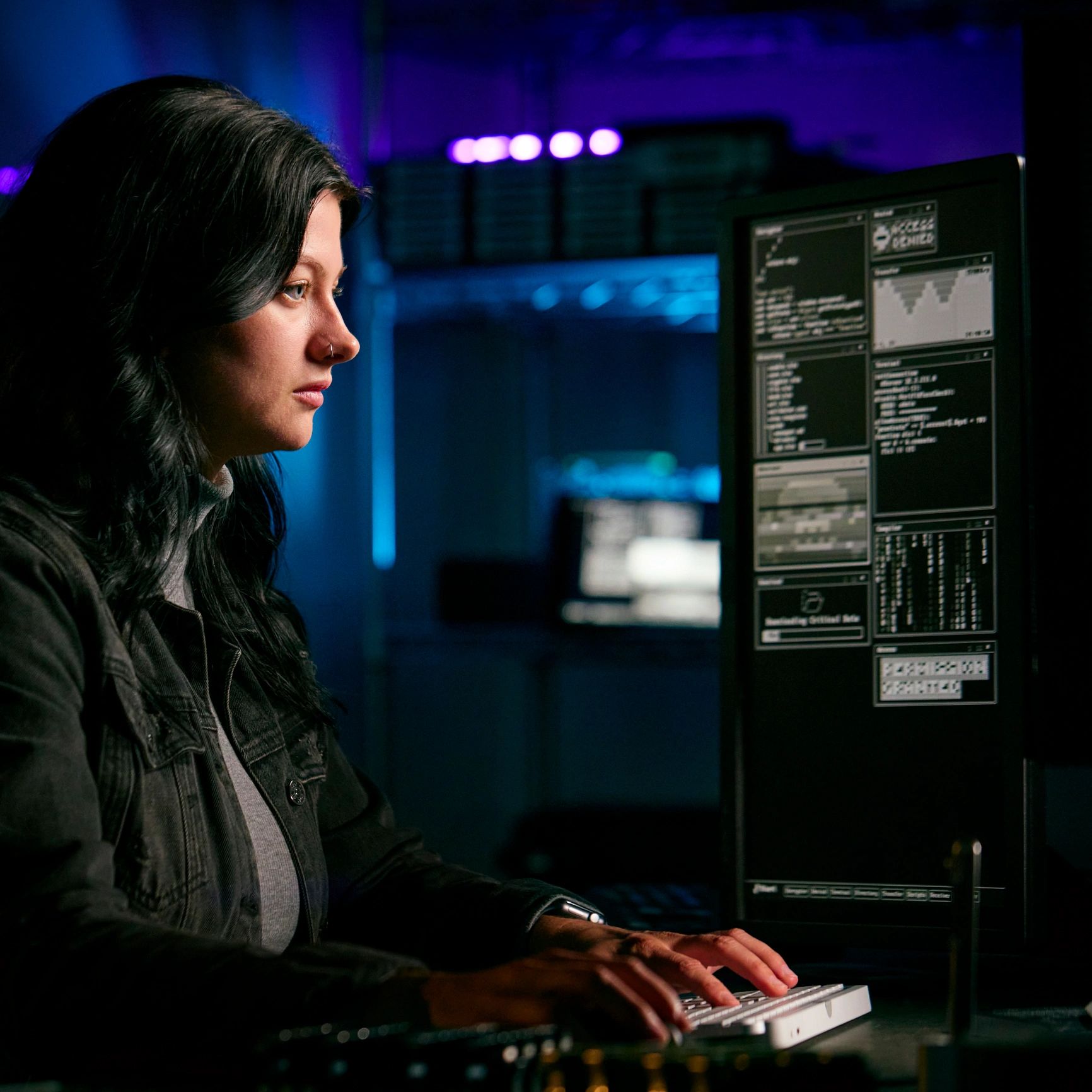 Woman focused on coding at computer in a dimly lit room.