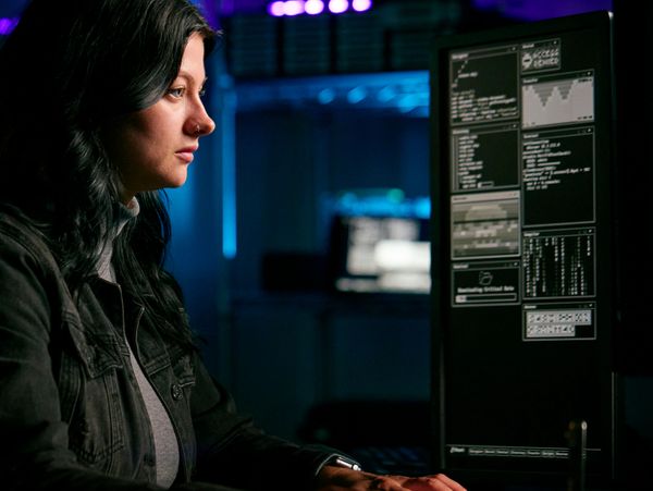 Woman focused on coding at computer in a dimly lit room.
