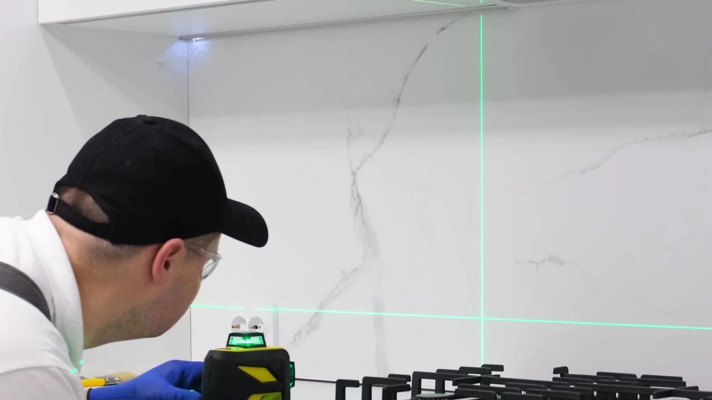 A worker uses a laser level to install a kitchen countertop with a stove.