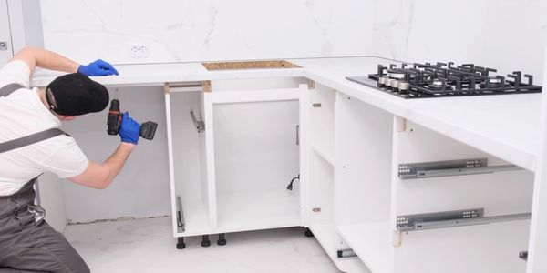 Worker installing white kitchen cabinets with a drill.