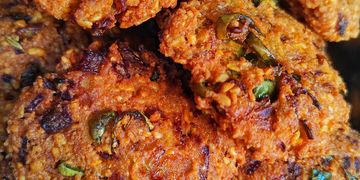 Close-up of crispy, golden-brown lentil fritters with green chili and herbs.