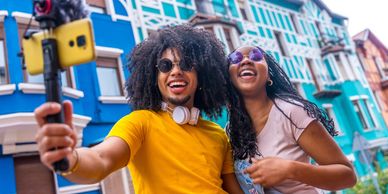 Two friends happily taking a selfie with colorful buildings in the background.