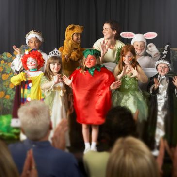 Children in costumes on stage bowing to the audience.