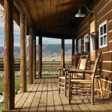 Rustic wooden porch with chairs overlooking a scenic mountain landscape.