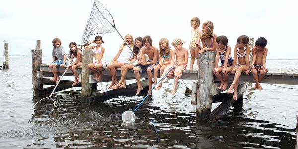 Group of children with nets sitting on a pier over water.