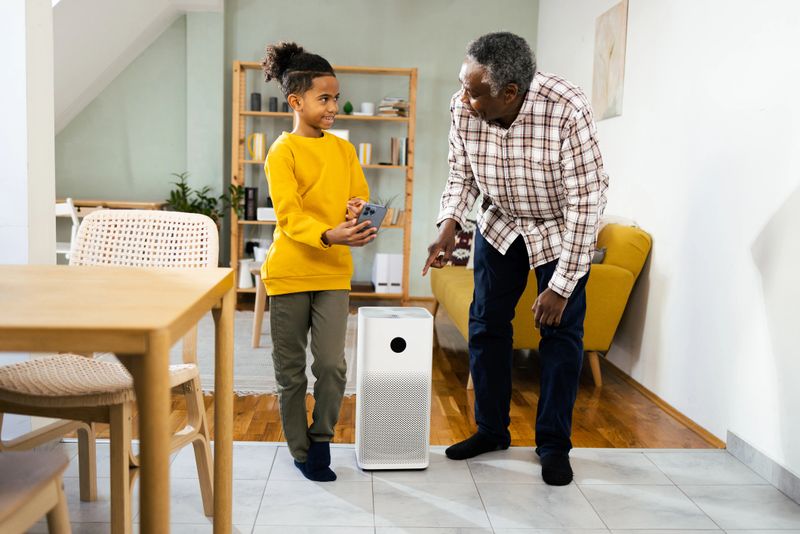 African American boy showing to his grandfather how to set up home air purifier, using smartphone.