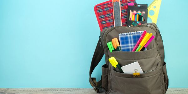 Backpack filled with colorful school supplies against a blue background.