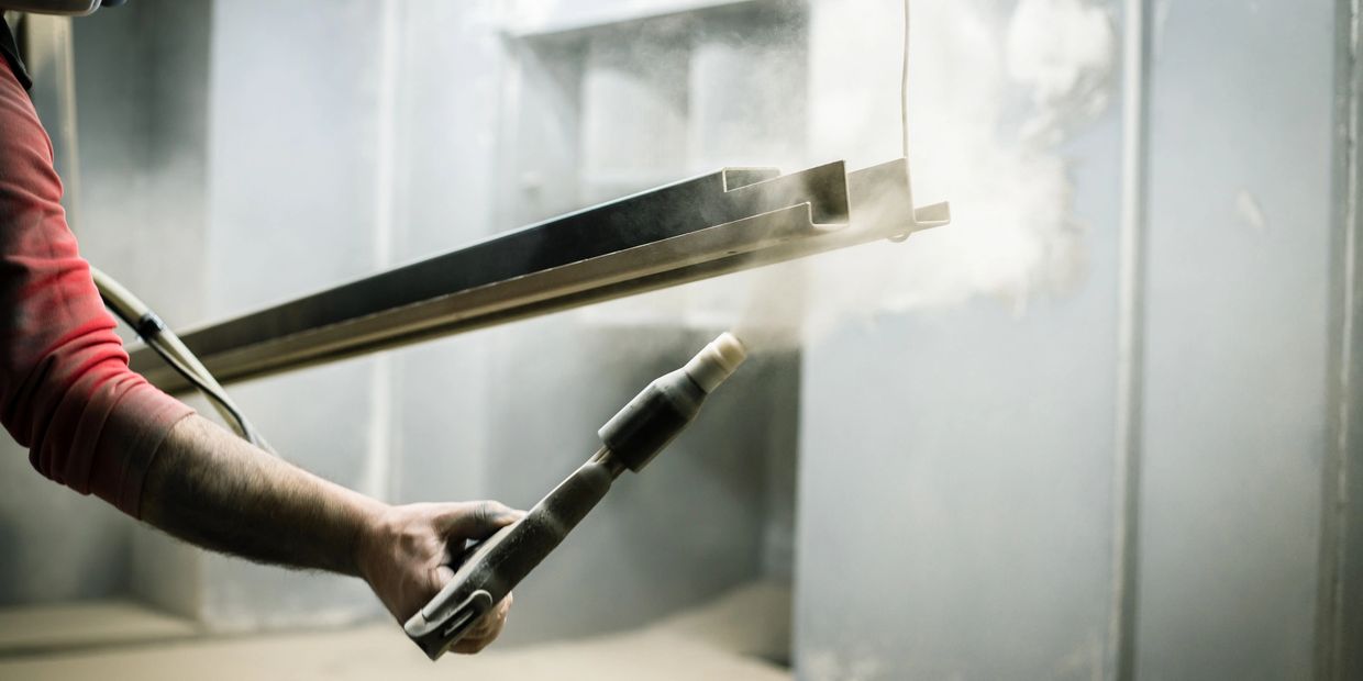 Worker applying powder coating to a metal part in an industrial setting.