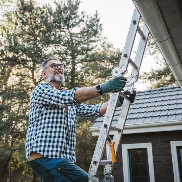Man in checkered shirt climbing a ladder outside a house.