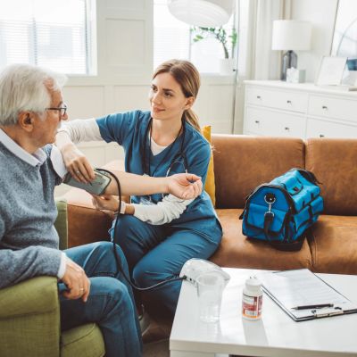 Nurse checks elderly man's blood pressure at home.