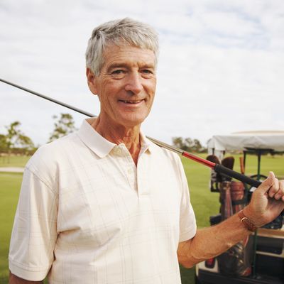 Senior man smiling with golf club over his shoulder on a golf course.